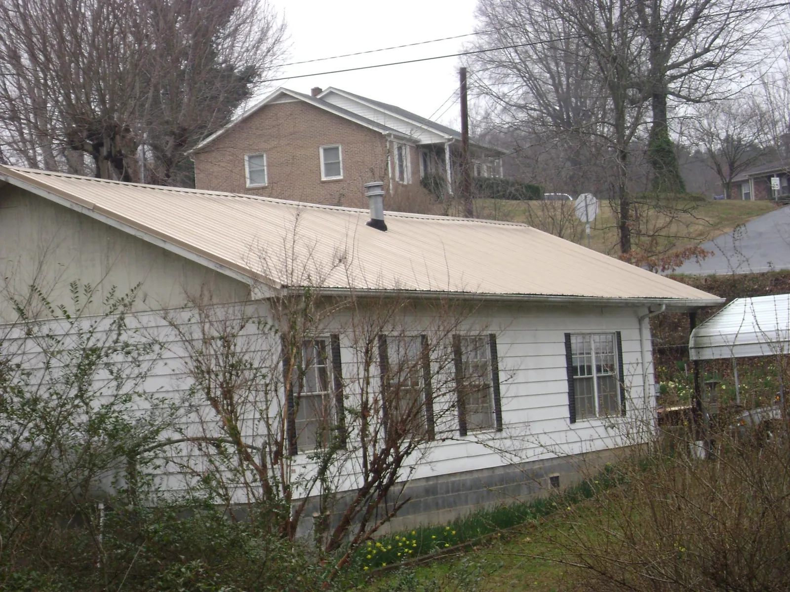 Tan metal roof on a white sided house set into a hillside — Commercial Roofing by Roofing Brothers in Greenville